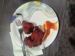 A plate with two pieces of deep-fried chicken food, accompanied by a serving of orange sauce. A fork rests on a napkin beside the food. The plate features a colorful, swirling pattern.