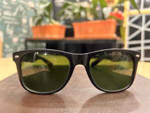 Black sunglasses with brown surface with blurry plants and geometric decorations in the background.