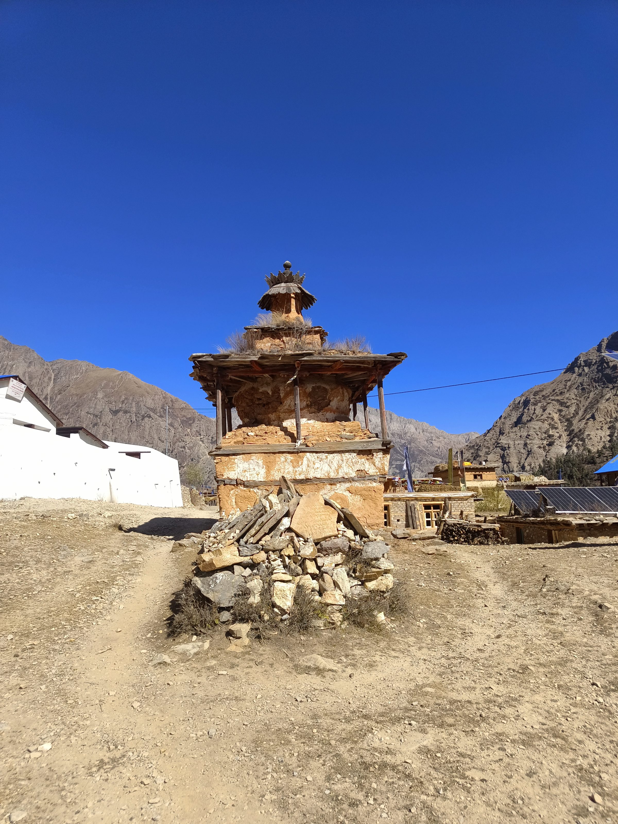 A traditional stone and mud structure with a tiered roof in a rural setting, surrounded by a mountainous landscape.