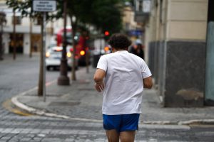 A person wearing a white t-shirt and blue shorts is jogging down a city street. 