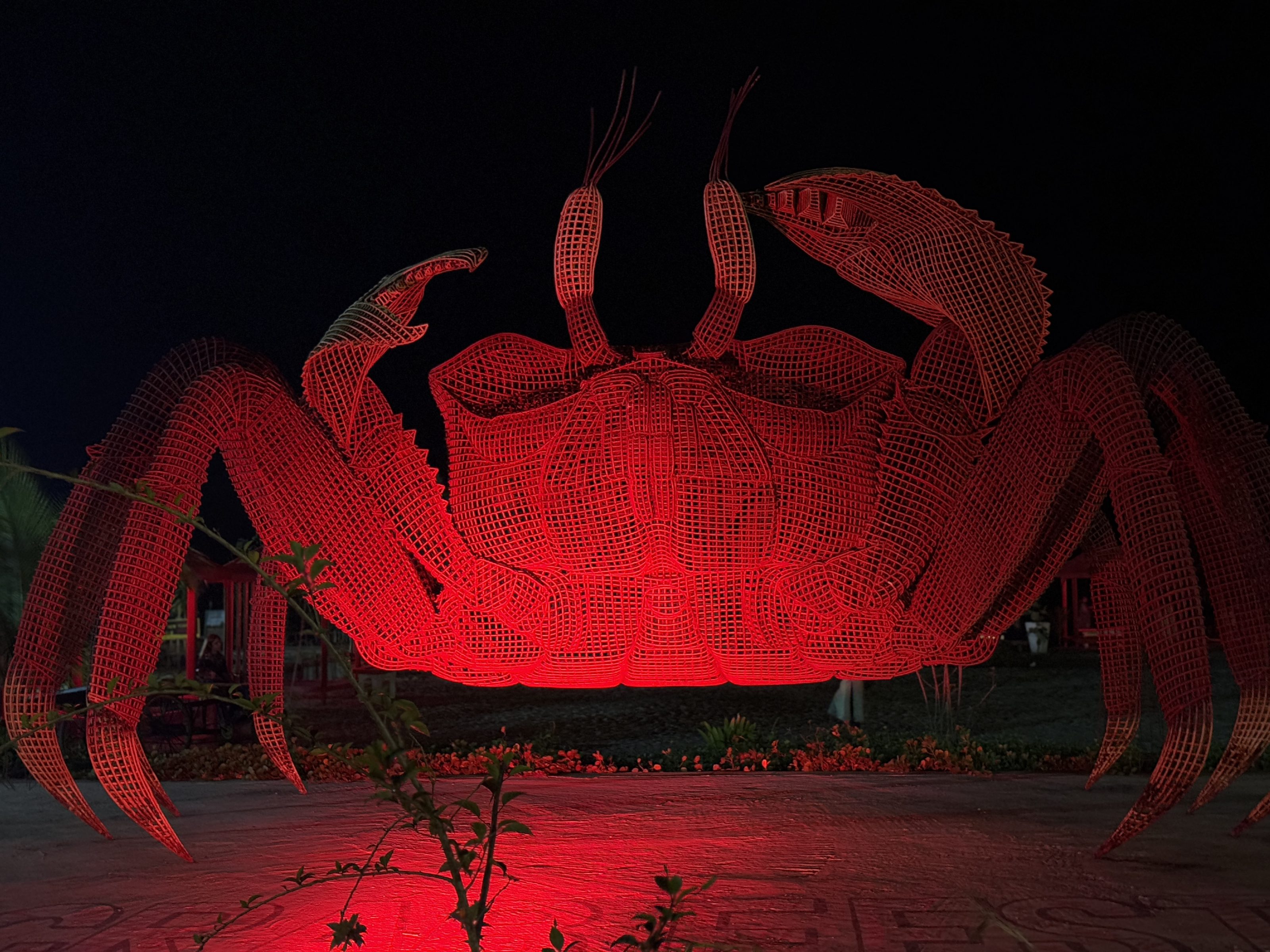 A large wireframe sculpture of a crab illuminated with red light, set against a dark background.