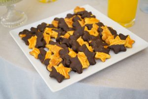 A white rectangular plate filled with star-shaped cookies partially dipped in chocolate, placed on a tablecloth.