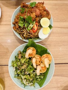 Two plates full of noodles, chicken, egg, lemon and some other vegetables. 