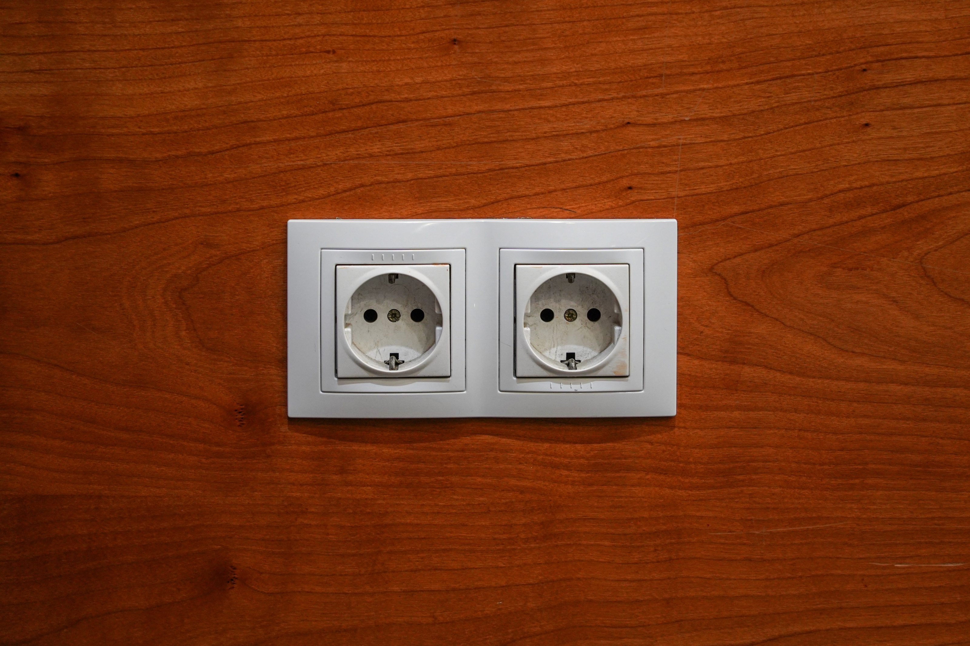 A pair of European-style electrical outlets mounted on a wooden wall.