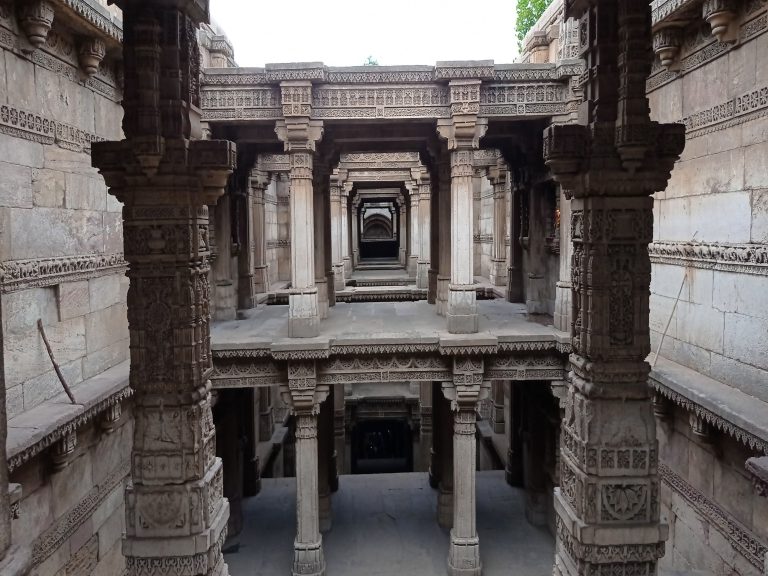 Historic Adalaj Stepwell in Gujarat, showcasing detailed stone carvings and a corridor that leads into shadowy depths.