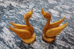 Two carved wooden duck figures with outstretched wings are placed facing each other on a textured stone surface.