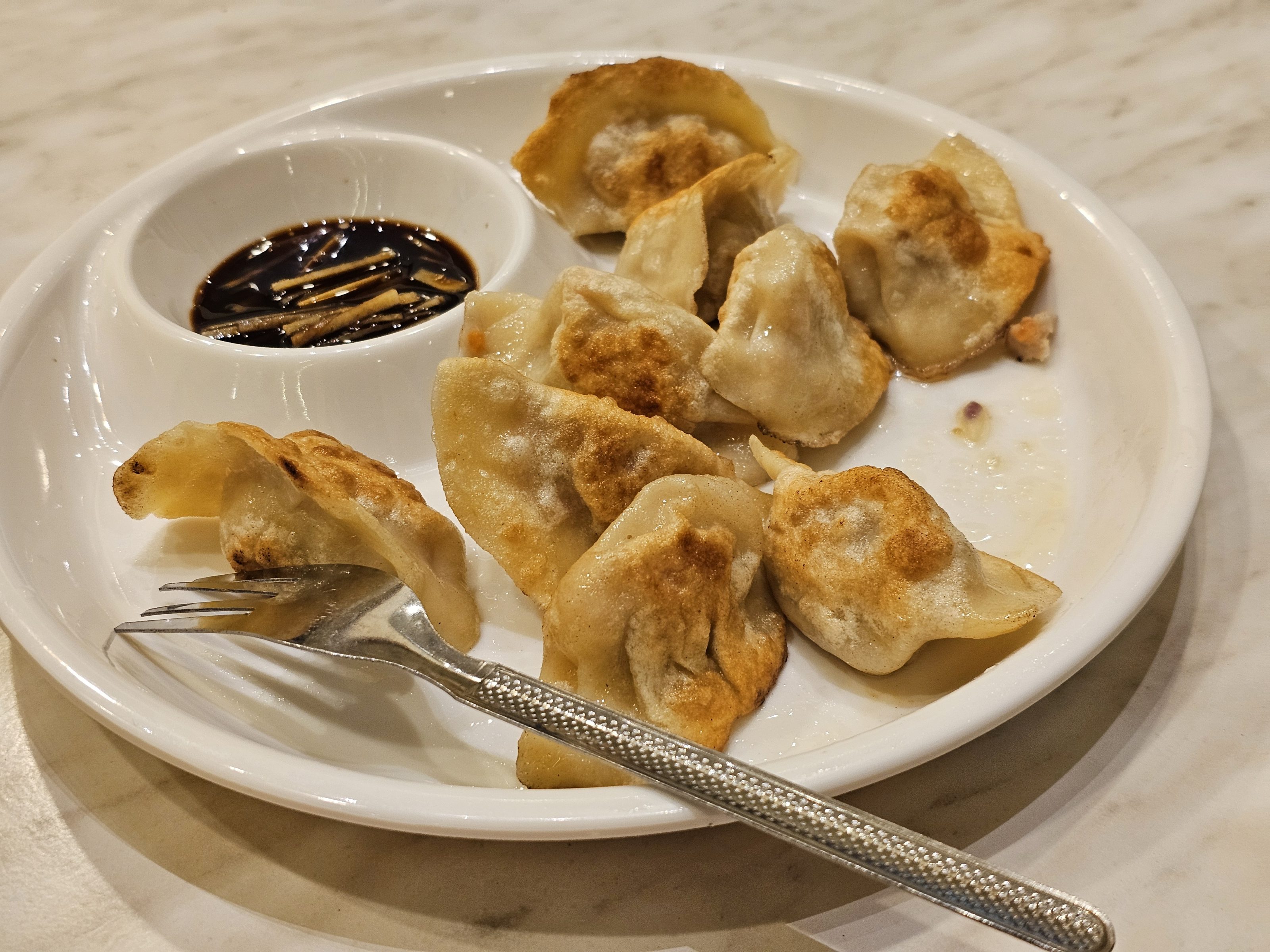 A plate with dumplings like food and soup in it. A fork is also there to eat. 