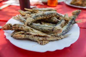 A plate of fried fish, served on a white dish with a red tablecloth in the background.