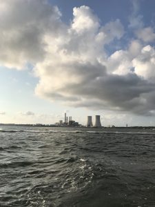 Large concrete cooling towers from the Brayton Point Station as seen from a boat on the Taunton River. The sky is overcast.