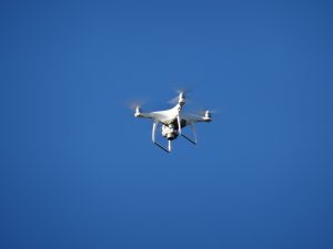 A white drone hovering mid-air against a clear blue sky