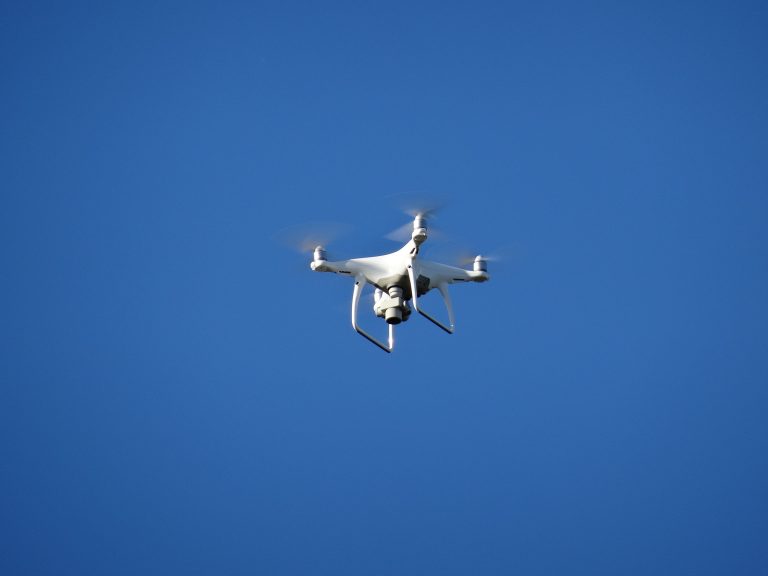 A white drone hovering mid-air against a clear blue sky