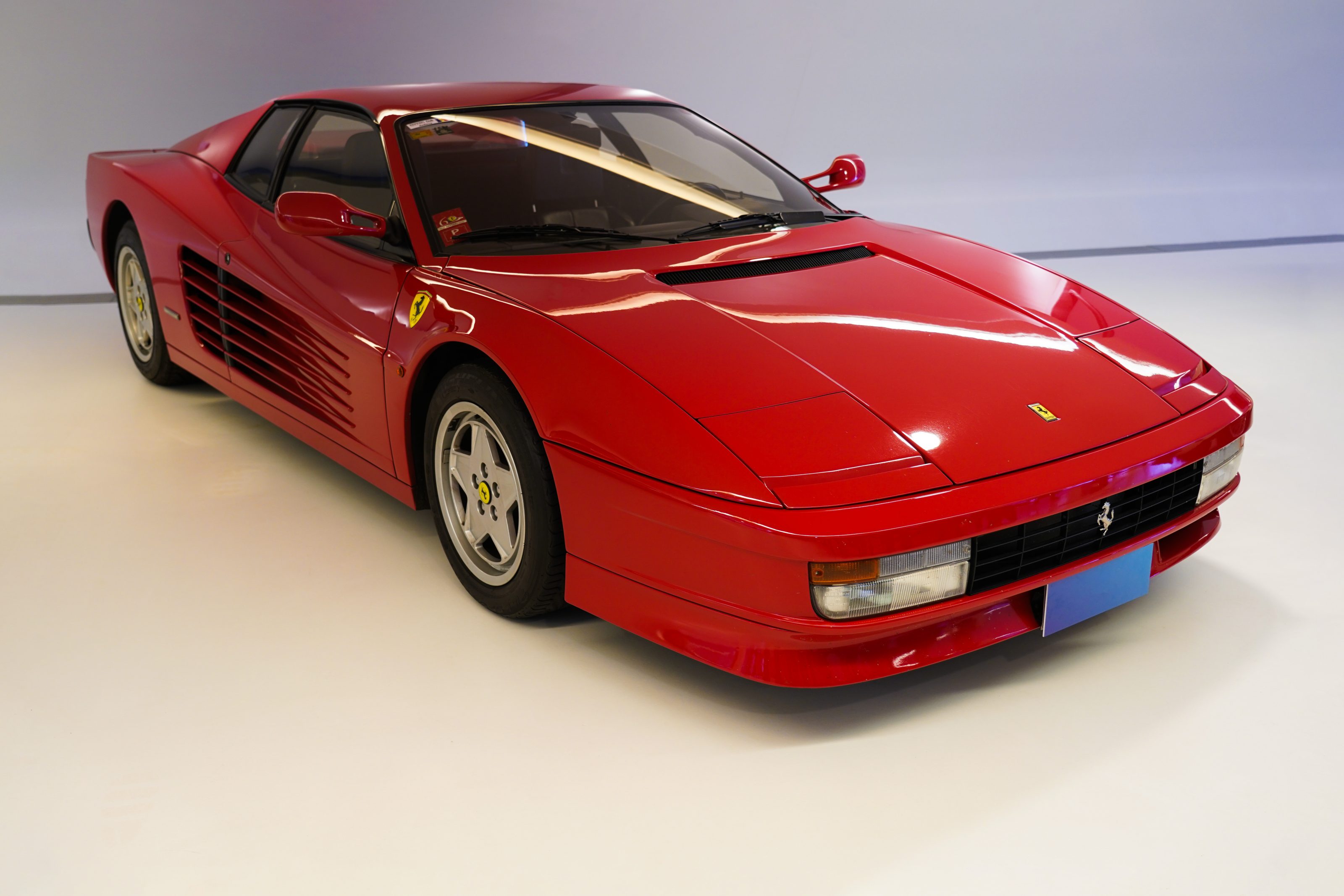 A red sports car with a sleek design and prominent side vents is displayed in a well-lit studio setting.