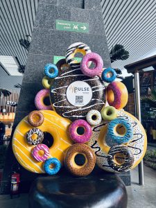 A colorful display of oversized, decorative donuts stacked against a dark stone wall.