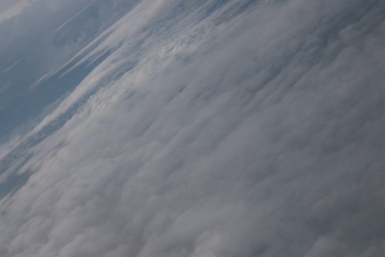 An aerial view of a thick cloud layer with varying shades of white and gray, captured from a high altitude, displaying the vast expanse of the sky.