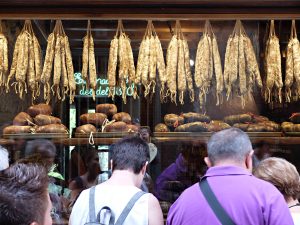 Shop window of a traditional Catalan sausage shop with several pieces hanging and some customers looking at the product