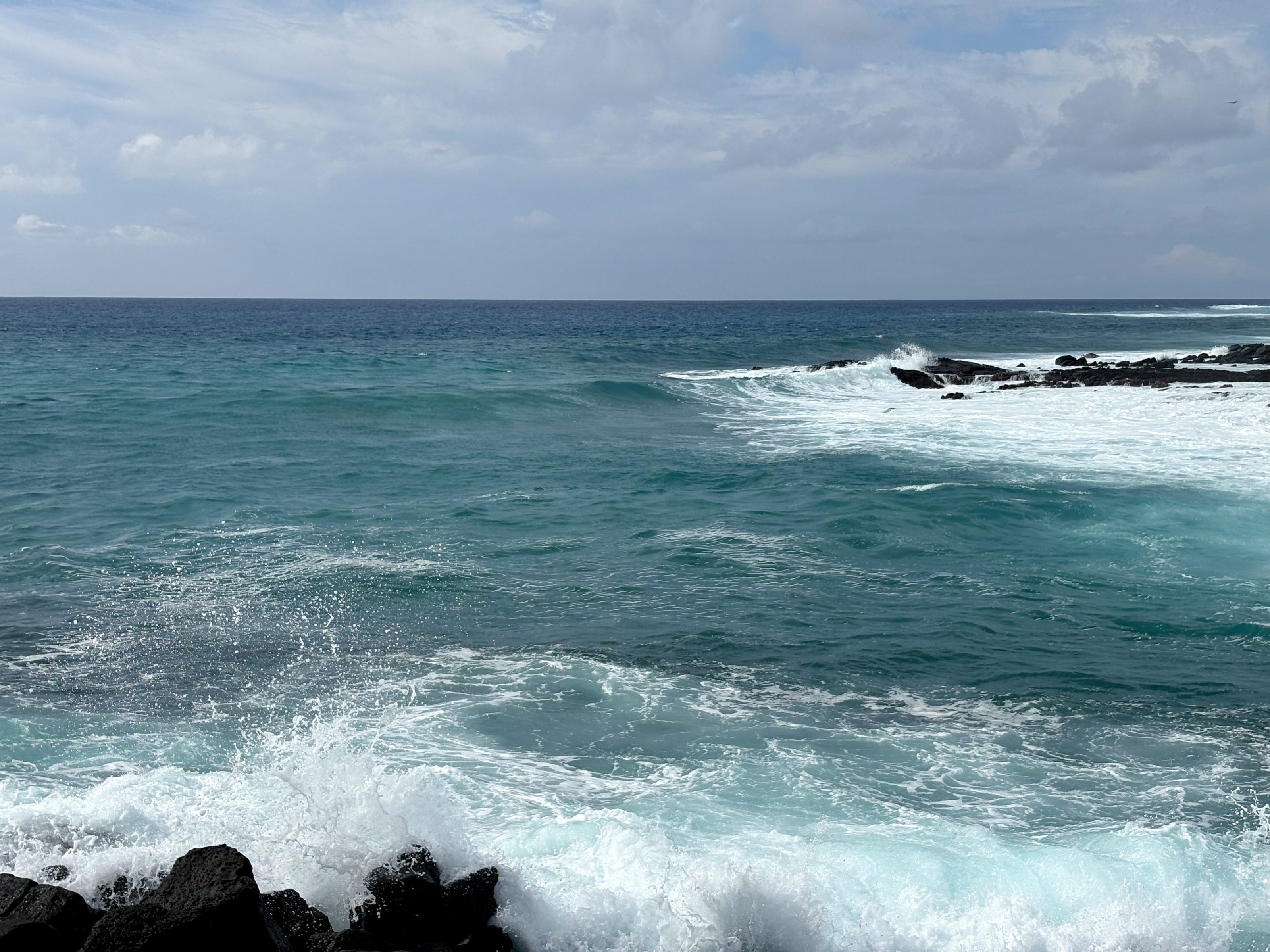 Blue waves crash against black lava rocks.