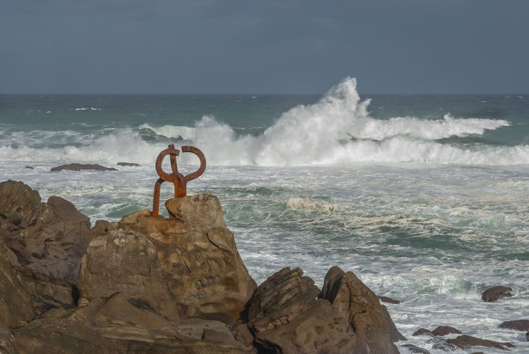 Iron sculpture “The Comb of the Wind” on the rocks of the coast of San Sebastian with a rough sea.