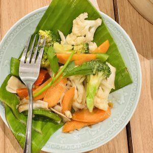 A plate full of veggies including cauliflower, broccoli, radish and mushroom. A steel fork is also there and those veggies are on the top of Banana leaf. 