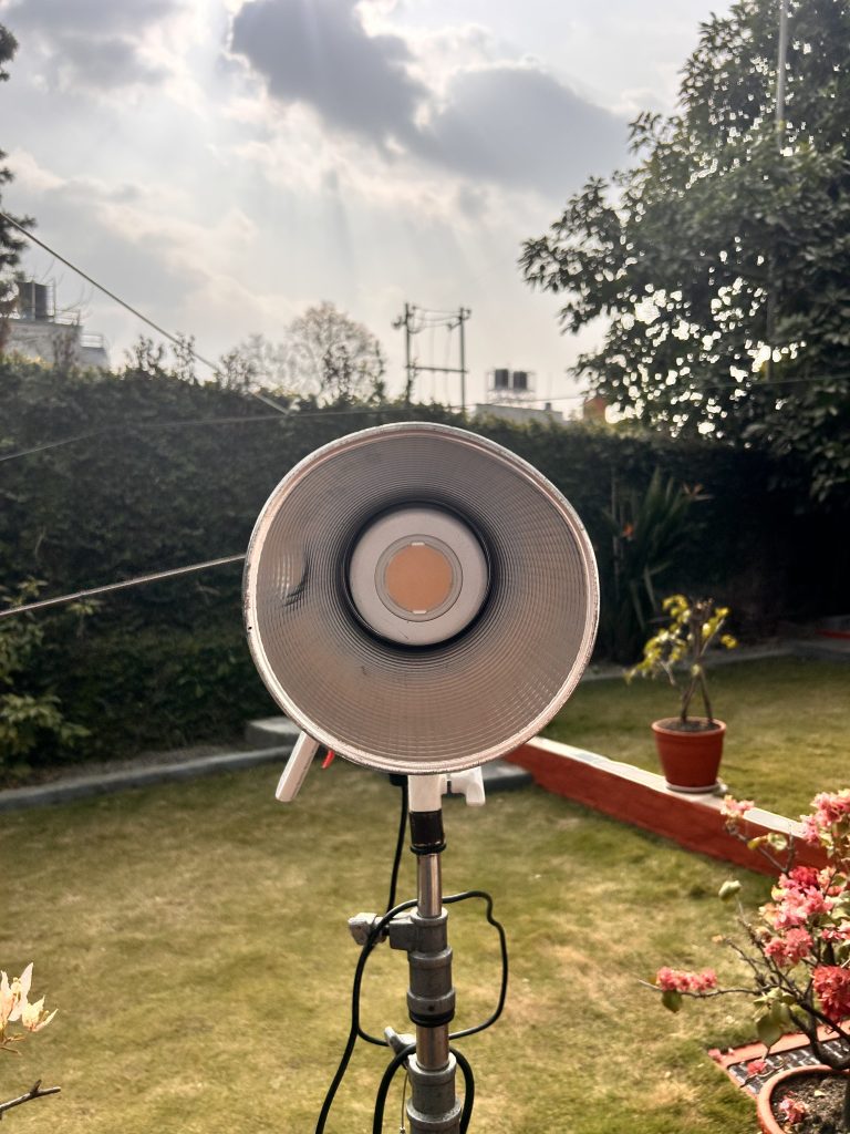 A outdoor studio light stands in a garden setting, with potted plants and a green lawn in the foreground.