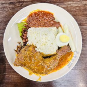 A plate full of white rice and a piece of Chicken in a restaurant in Malaysia. 