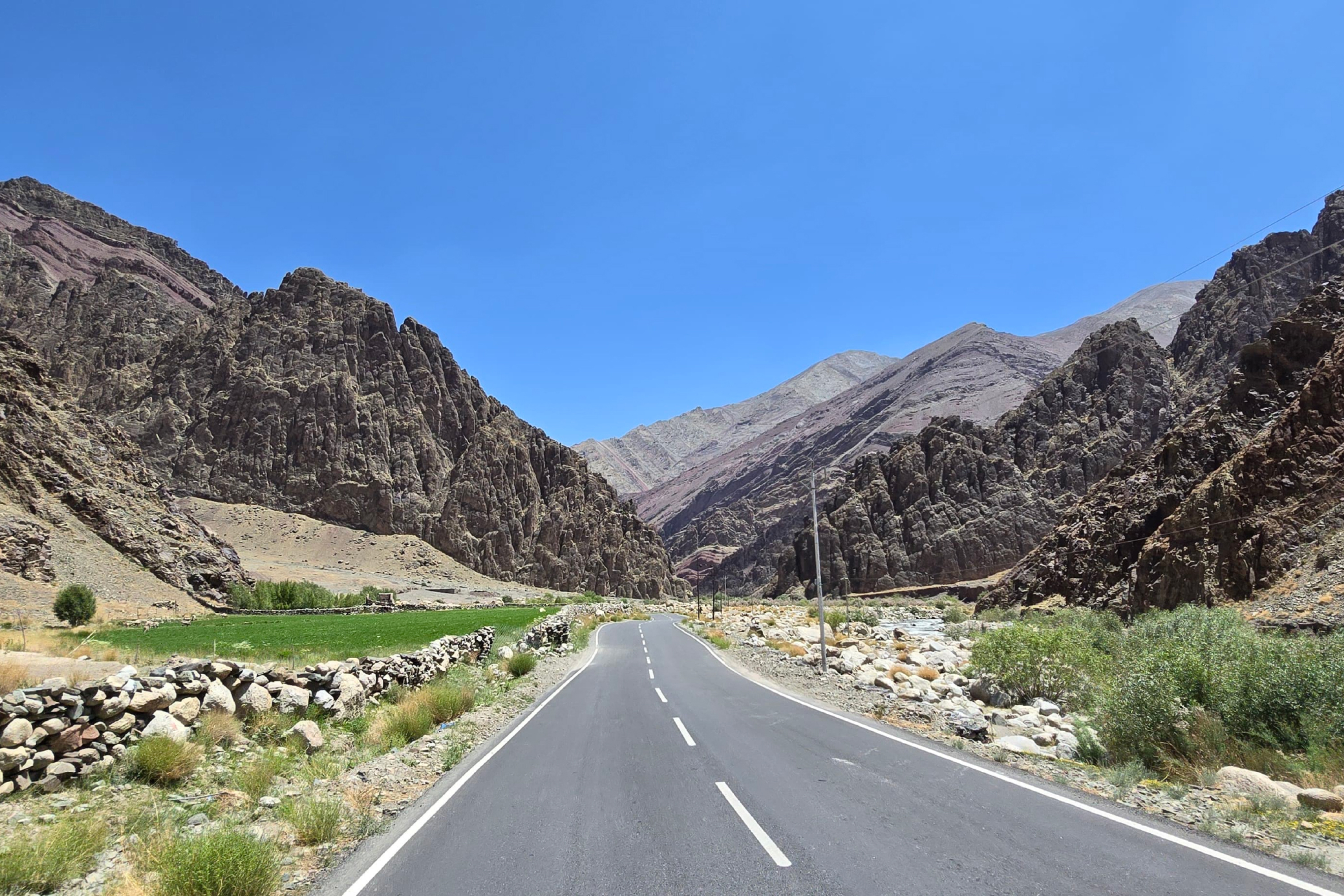 A paved road leads through a rocky mountainous landscape under a clear blue sky.