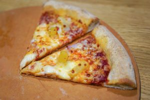 Two slices of delicious pizza with cheese and delicious pineapple on a wooden surface, served at a Wordpress Meetup