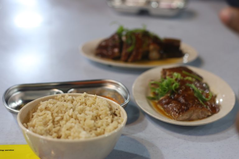 A white bowl filled with fluffy, cooked rice, placed on a neutral background,  A simple white bowl containing steaming white rice, showcasing its texture and color.