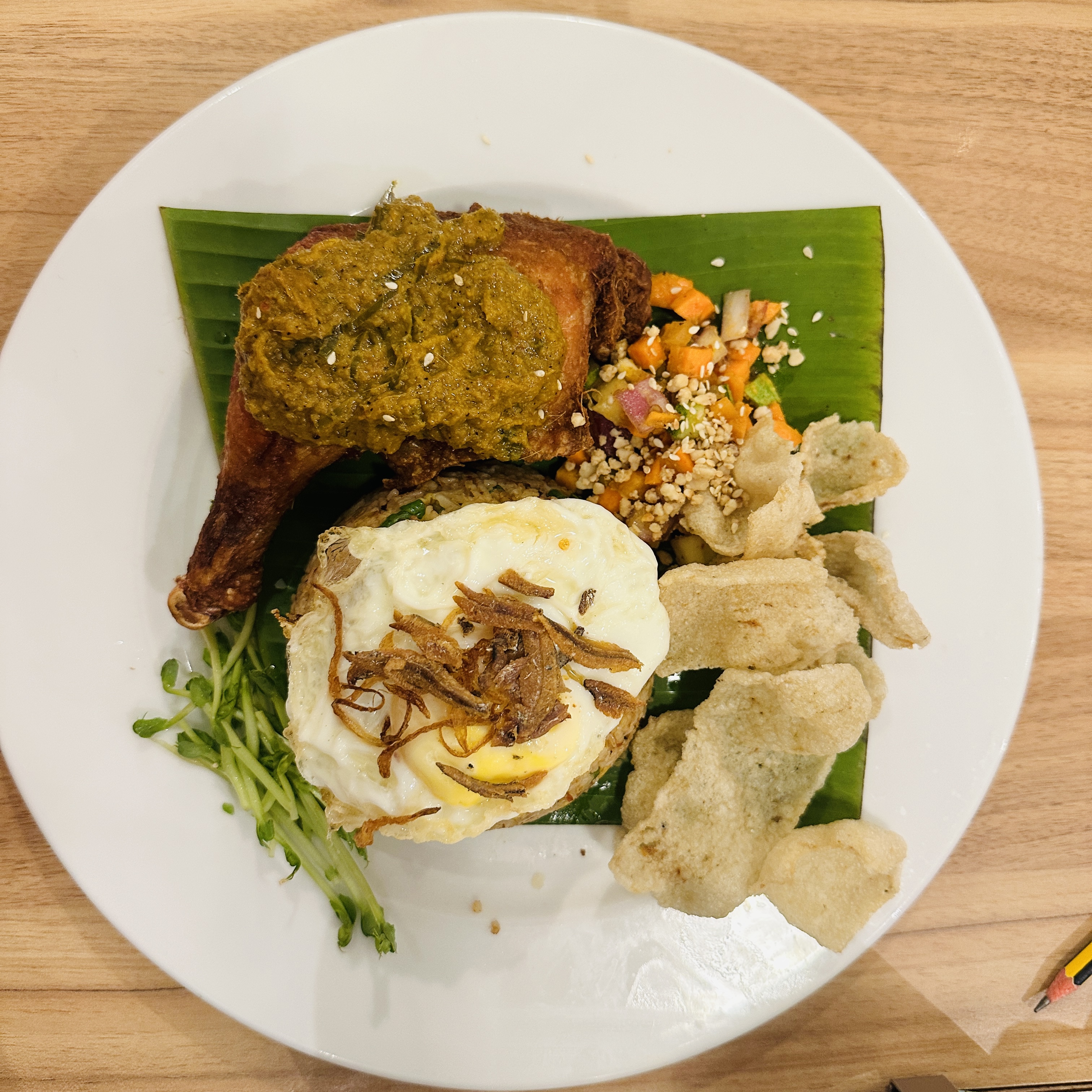 A plate having yellow rice and is covered with an omelette, chicken pieces, fries and some vegetables.