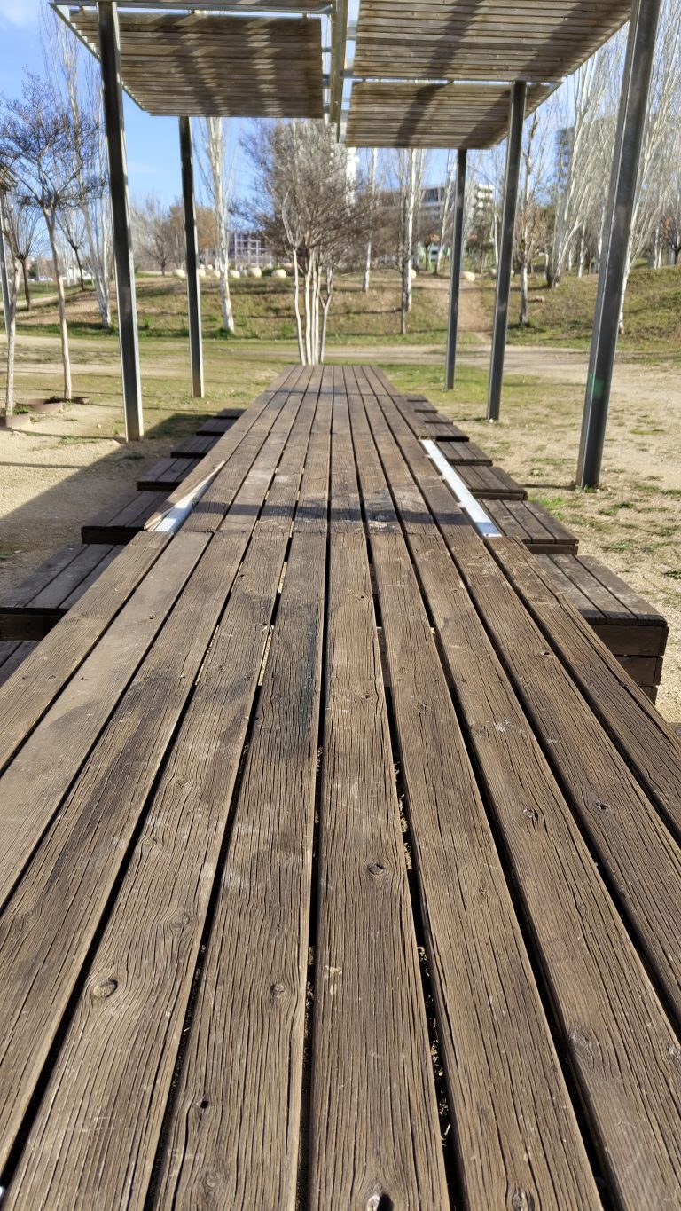 Low-angle shot of a wooden platform in an urban park, featuring weathered wood texture and shaded structures.