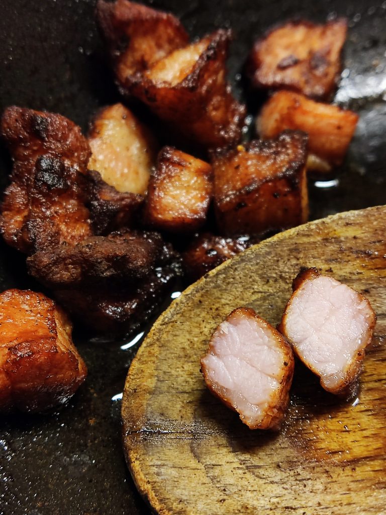 Well-fried thick bacon cracklings, one cut and placed on a wooden spoon