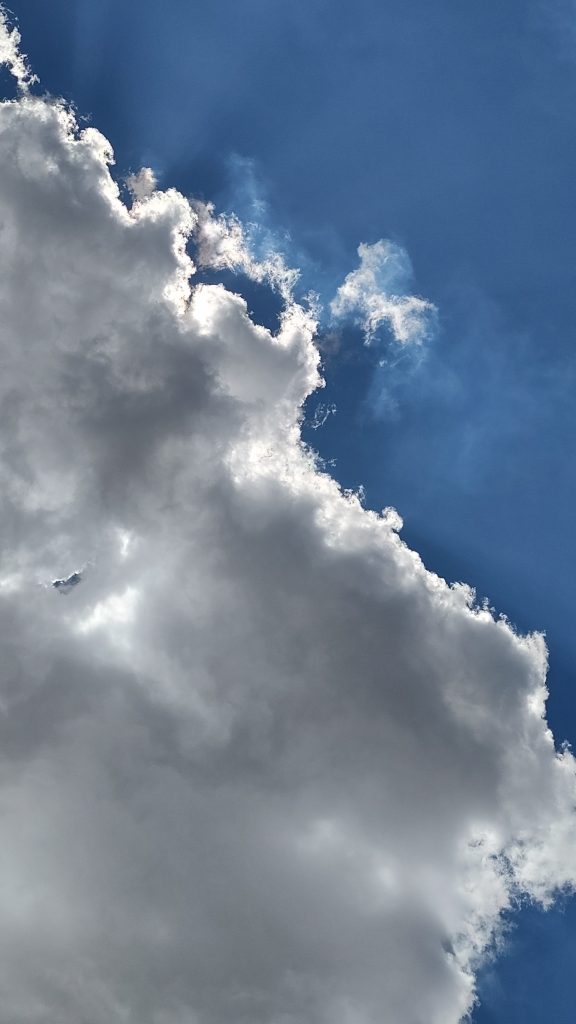 A bright and fluffy cloud against a deep blue sky, with sunlight illuminating the edges.