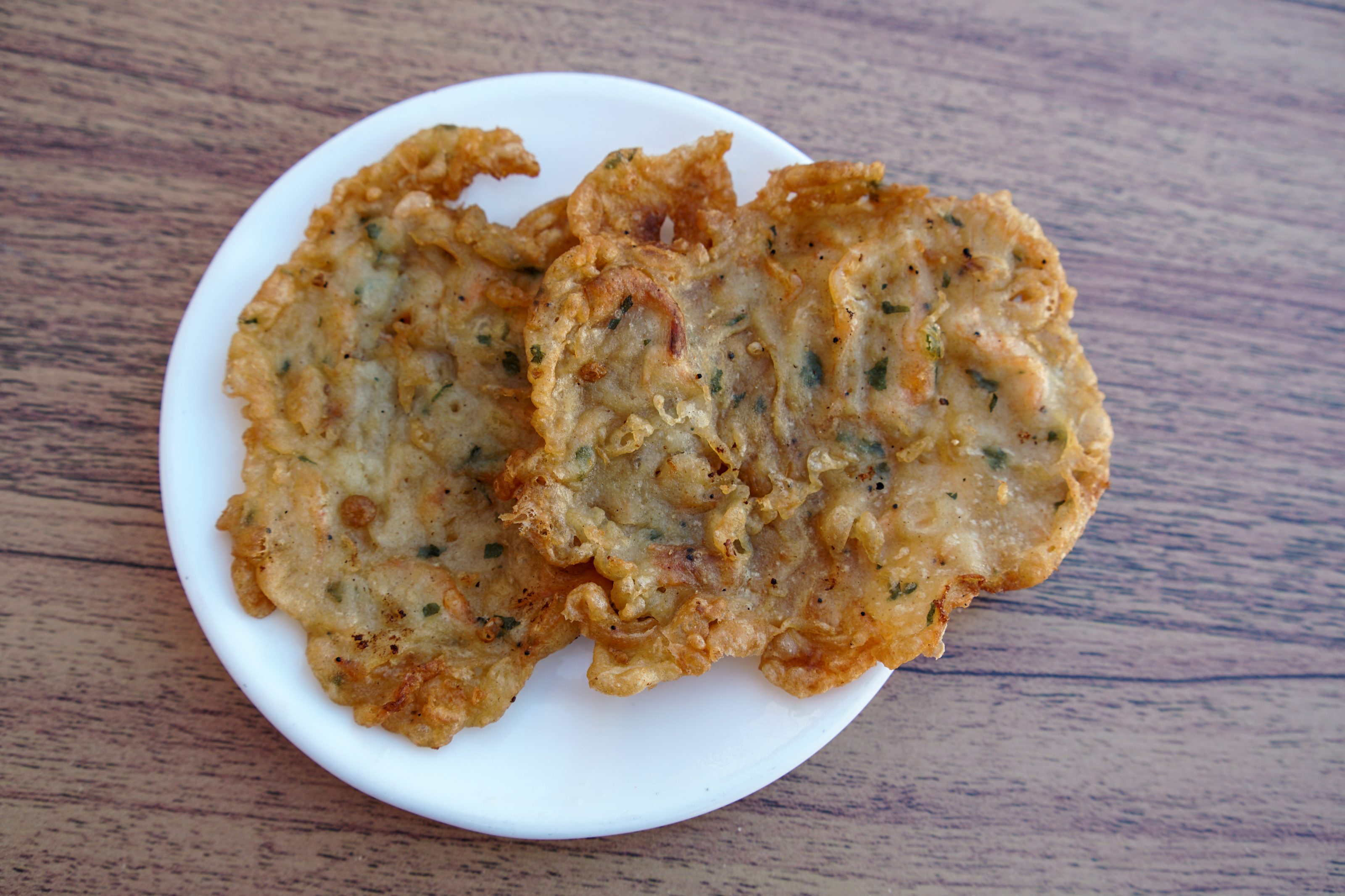 Two tortillitas de camarones, pieces of crispy, fried shrimp fritters on a white plate, placed on a wooden table.