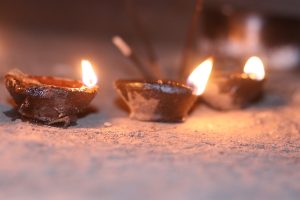 Three small clay oil lamps with flames, placed on a sandy surface, creating a warm and serene ambiance.