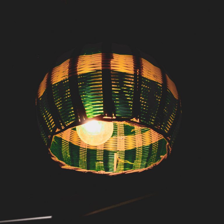 A hanging lamp with a woven wicker shade, featuring green and yellow stripes, illuminated in a dimly lit setting.