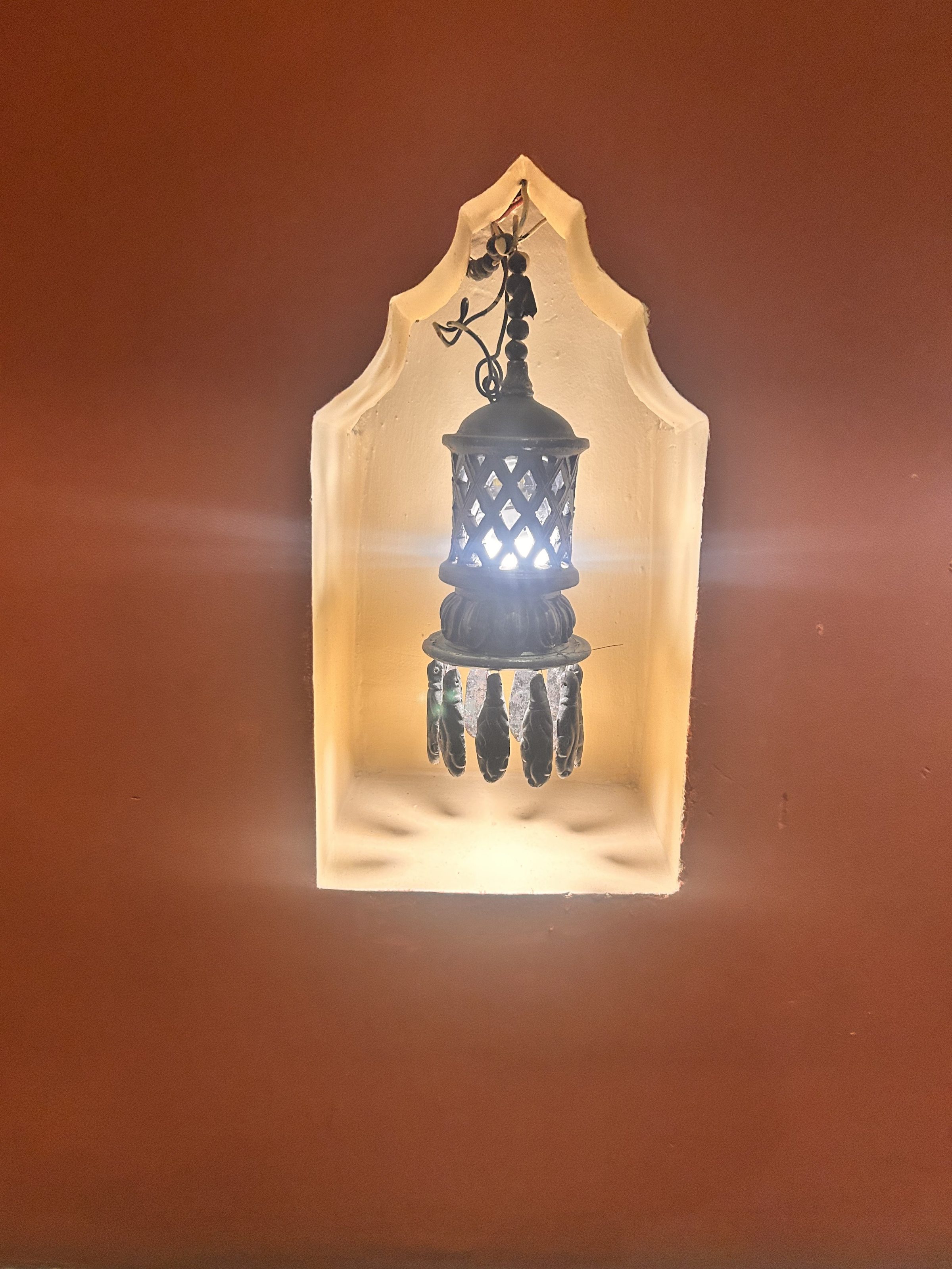 A decorative lantern with intricate cut-out patterns is illuminated, casting a warm light in a recessed niche with an ornate frame.