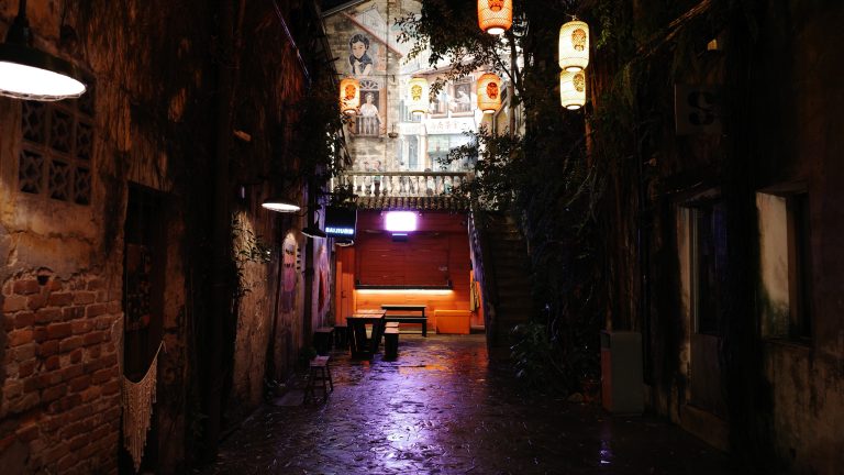 A narrow alleyway featuring a bench illuminated by soft lights, creating a serene and inviting atmosphere.