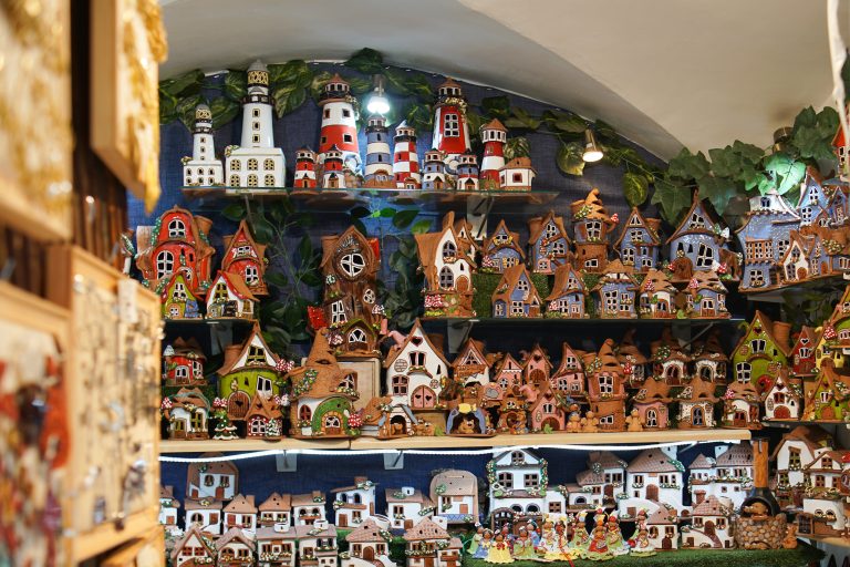 Display of colorful, handcrafted ceramic houses and lighthouses on shelves.