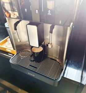 A coffee machine dispensing coffee into a black mug placed on the drip tray.