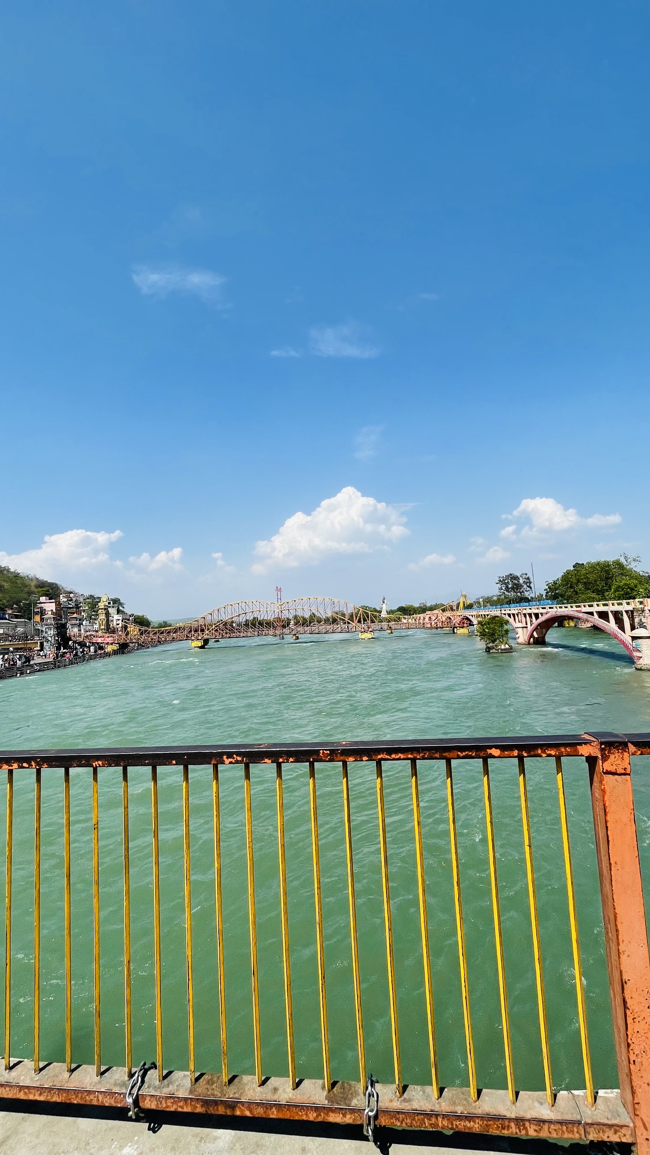 A scenic view of a wide river with a bridge crossing over it. The river is surrounded by buildings on one side and greenery on the other. 