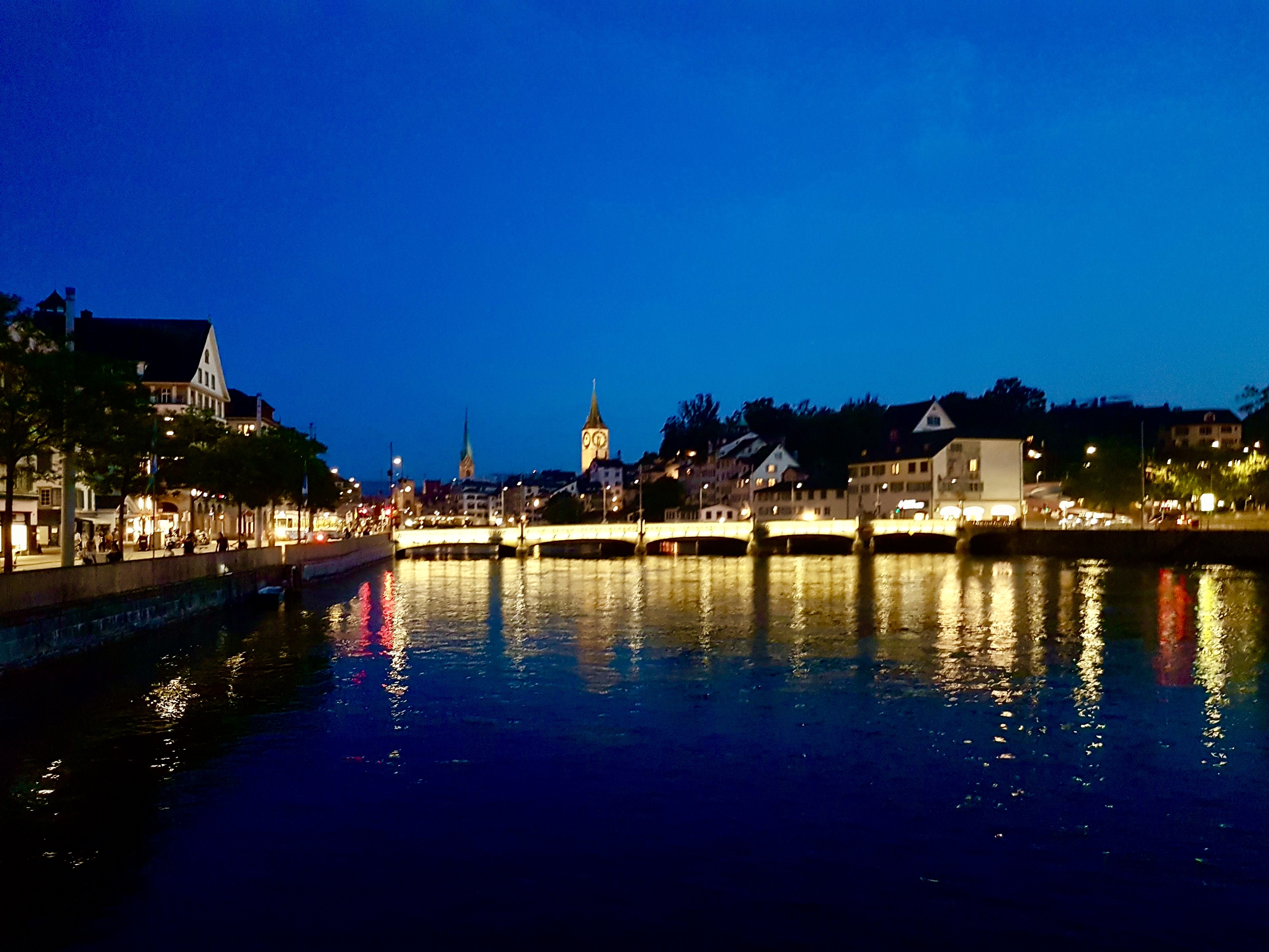 A serene night view of a river reflecting city lights and buildings along its banks, creating a tranquil atmosphere.