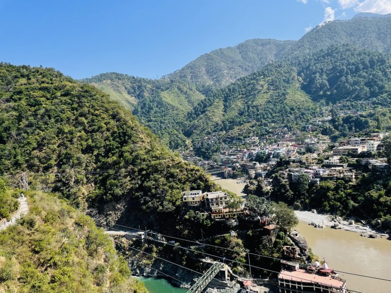 Scenic view of a mountain town with lush green hills, a river, and a suspension bridge