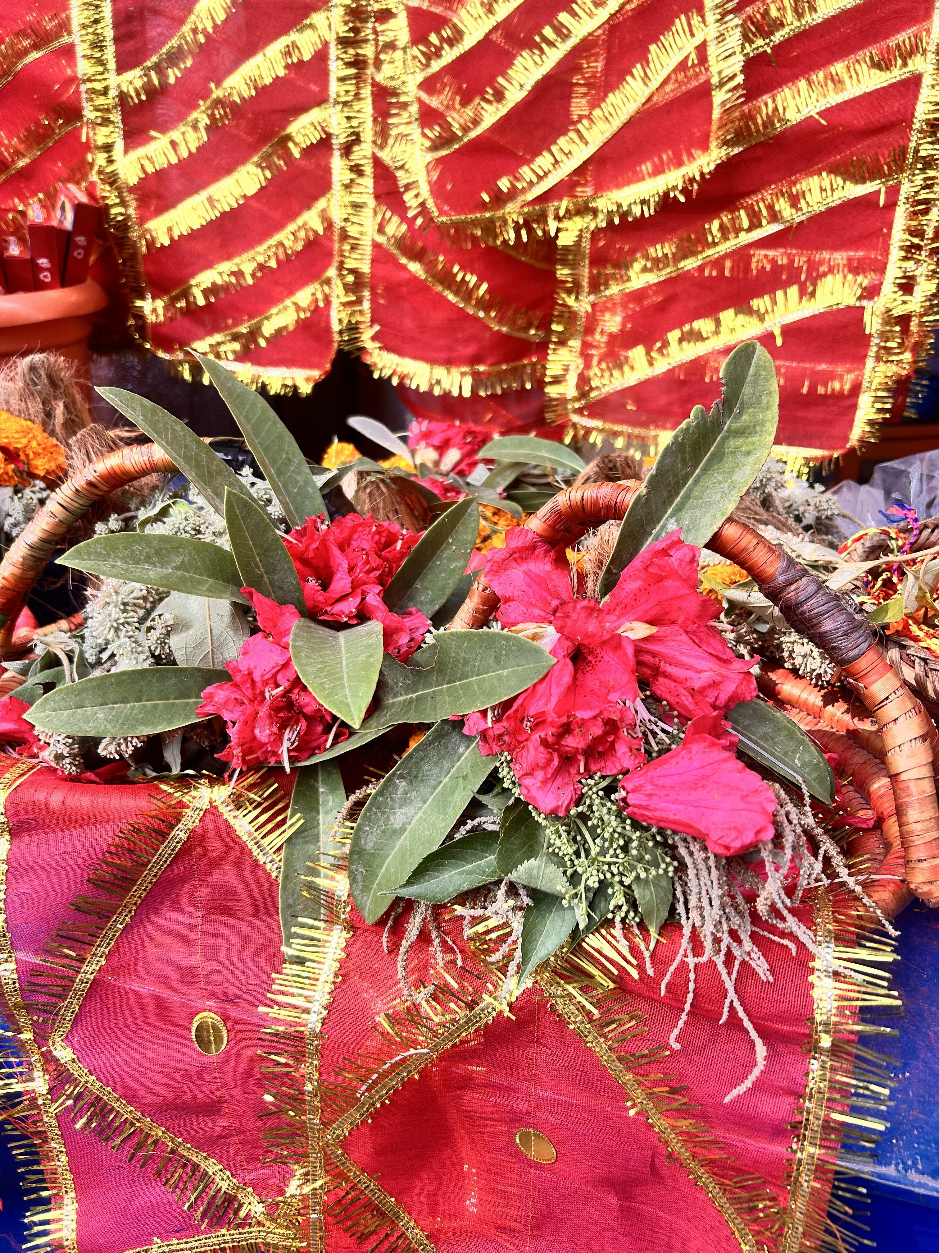 A decorative basket filled with lush red flowers and green leaves, set against a vibrant background of red fabric adorned with golden fringe and foil designs.