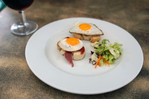 Small toasts with fried quail eggs and Iberico ham with a side of salad. There is a glass of wine in the background.