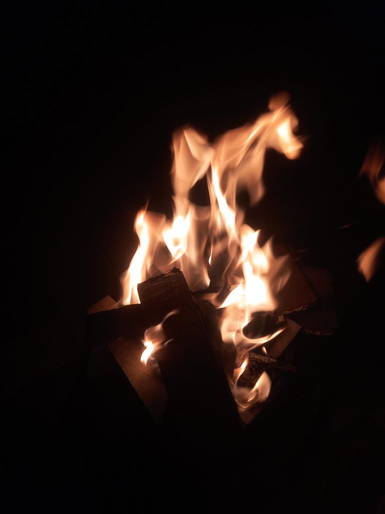 A close-up view of a campfire with brightly burning flames against a dark background.