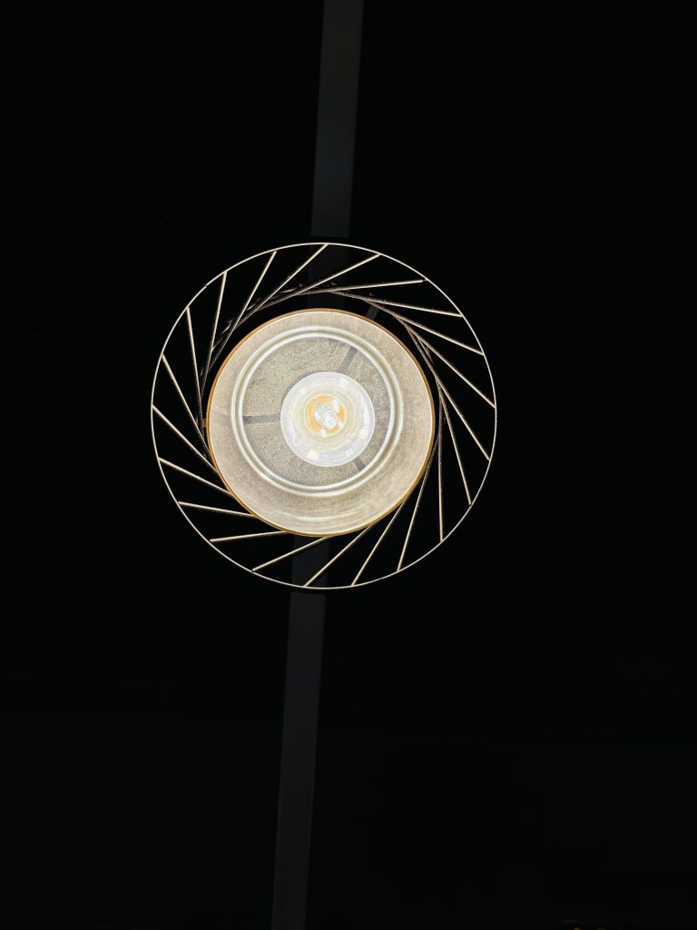 A close-up view of a decorative ceiling light fixture with a circular design, featuring intricate geometric patterns in the surrounding rim, set against a dark background.