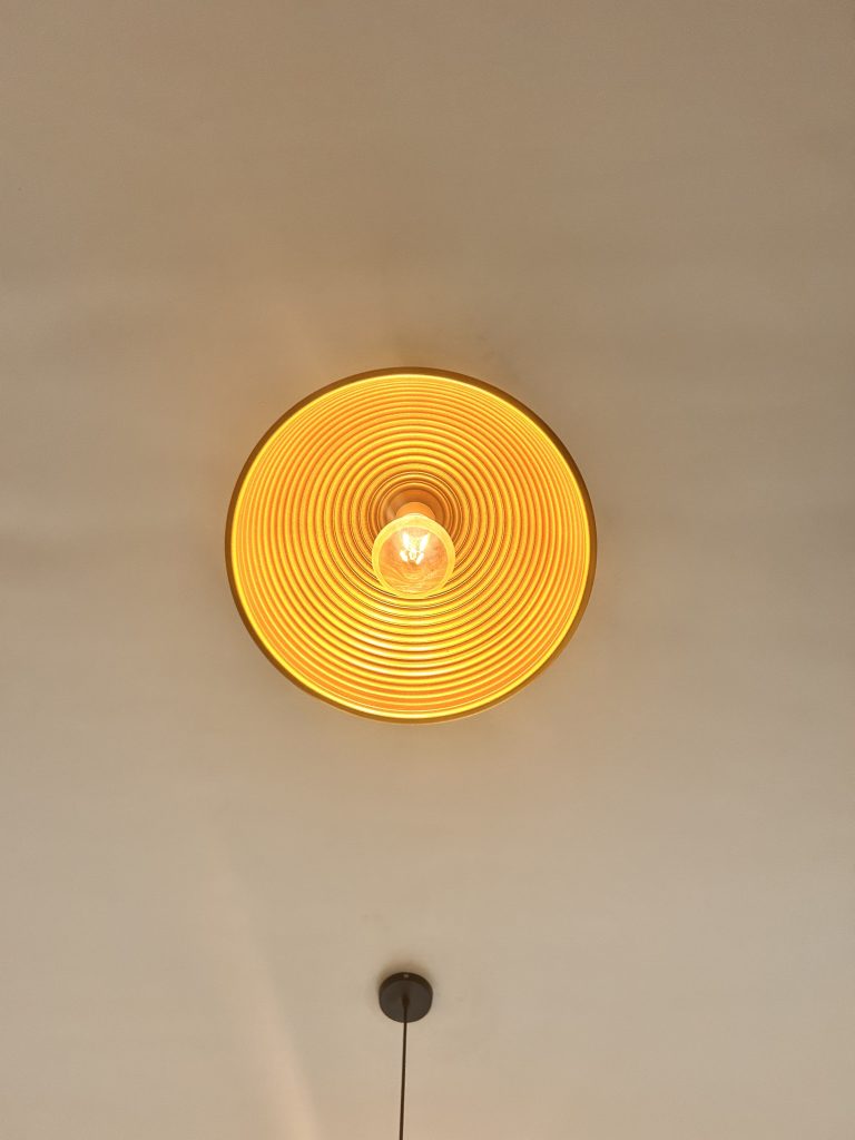 A ceiling-mounted circular light fixture with a glowing bulb and concentric design on its surface, casting a warm orange glow.