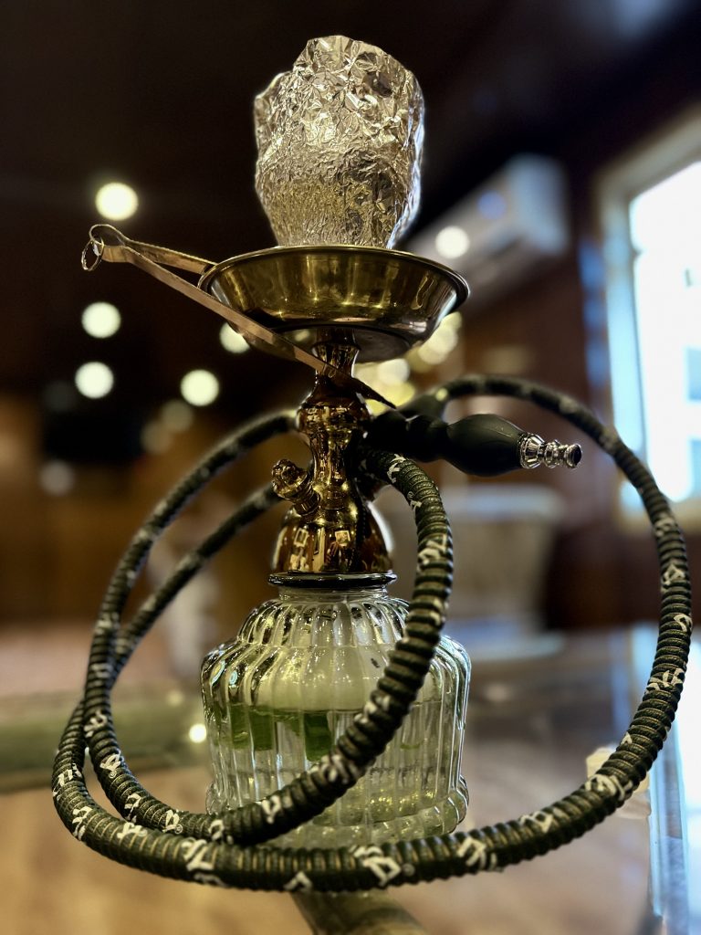 A close-up of a hookah with a detailed metal stem and a patterned hose coiled around it.