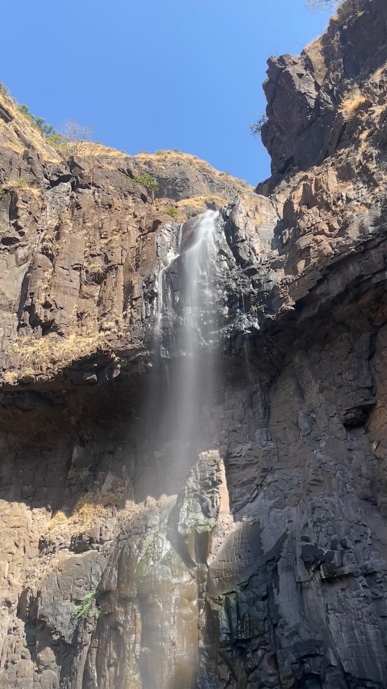 A waterfall cascading down a steep rocky cliff against a clear blue sky.