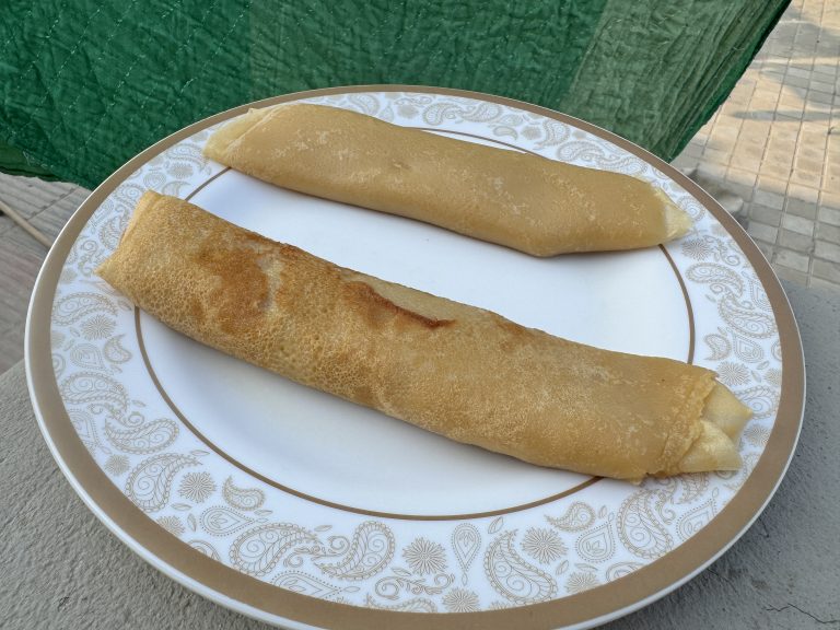 Two crispy dosa rolls served on a decorative white plate with gold paisley border pattern, one appears more golden brown than the other.