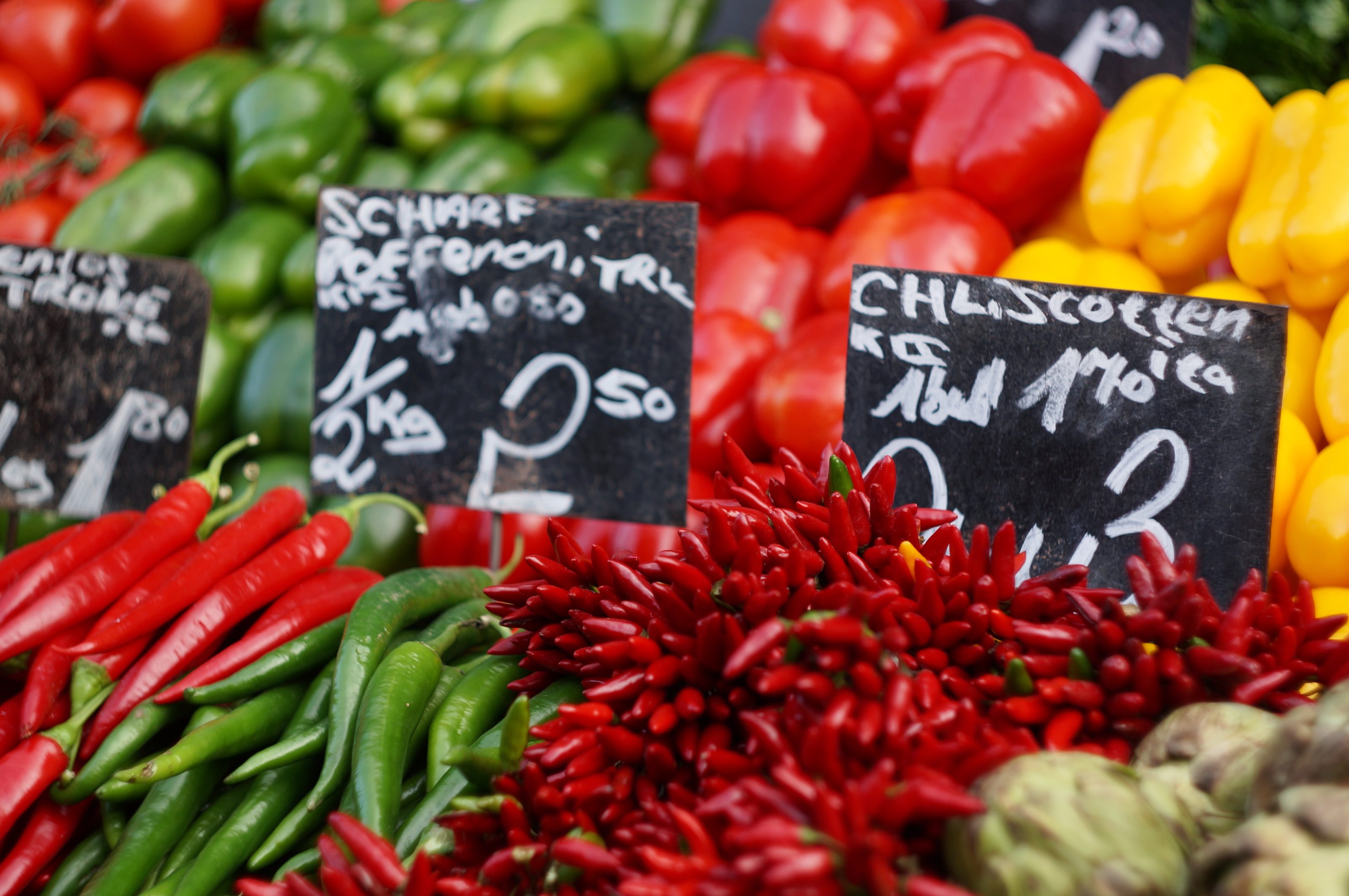 Counter with green peppers, yellow peppers and chili peppers and in a market.